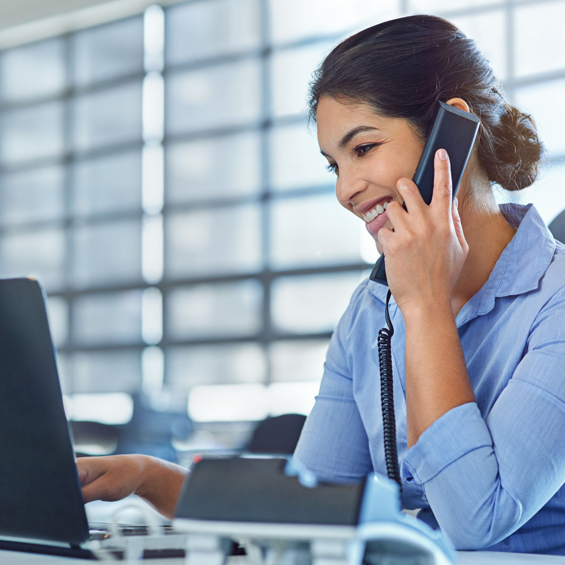 Shot of a young businesswoman talking on the phone while using a laptop at work